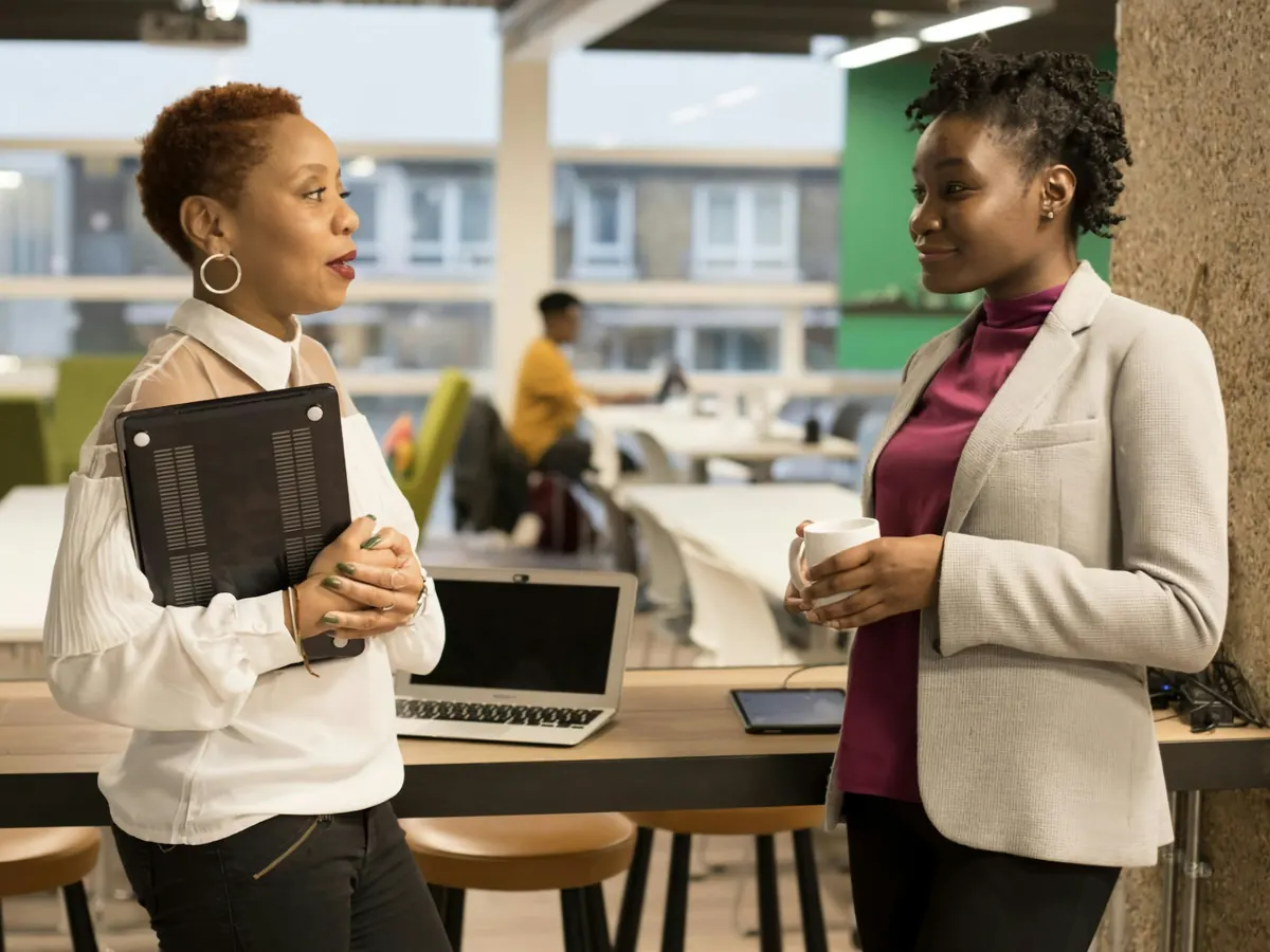 Two colleagues talking over coffee in a bright open-plan office